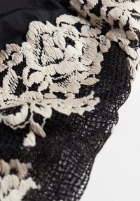 Svart tyg med beige blommig broderi, med texturerade detaljer och intrikata spetsdetaljer vid kanterna.