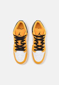 Gula och vita sneakers med svarta snören, som har en perforerad tåbox och logodetaljer. Tillverkade av läder och mesh-material, lågskurna design.