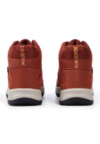 Punaiset vaelluskengät, joissa on teksturoitu verkko-osa, pehmustettu kaulus ja kontrastiväri beige pohja. Takana keltaista tikkausta.