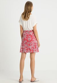 Gonna rossa a fiori con motivi a foglia bianchi, realizzata in tessuto leggero, presenta un design svasato, lunghezza media e una vita elasticizzata.