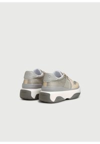 Sneakers hebben een beige en grijs mesh bovenwerk met een gestructureerde afwerking, een dikke witte zool en subtiele branding aan de achterkant.