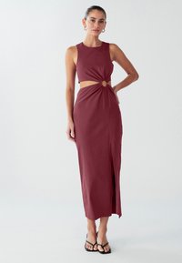 Mauve krāsas maxi kleita ar pieguļošu korpusu, izgriezumiem, savītu priekšu ar apaļu akcentu un sānu šķēlumu papildu kustībai.