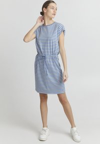 Csíkos kék ruha rövid ujjakkal, rugalmas derékkal és húzózsinórral. Puha anyagból készült, fehér sportcipővel párosítva.