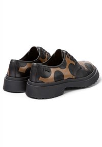 Chaussures en cuir noir et marron avec de grands motifs circulaires, bout rond, design à lacets et semelle en caoutchouc épaisse avec une finition texturée.