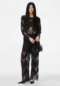 Černý dlouhý top s krajkou na rukávech a široké kalhoty se vzorem květin. Doplněno černou kabelkou se stahovací šňůrkou a špičatými botami.