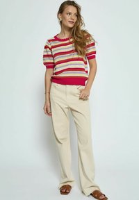 Gestreifter Pullover mit pinken, gelben und weißen Streifen, kurzen Puffärmeln und gewelltem Ausschnitt; kombiniert mit beigen weit geschnittenen Hosen und braunen Sandalen.