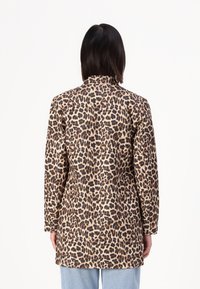Palton cu imprimeu leopard, cu mâneci lungi, tăiat drept, textură a țesăturii similară cu blana, având pete negre și maronii pe un fundal bej.