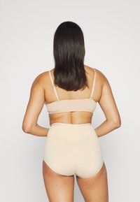 Set di reggiseno beige senza cuciture e mutandine a vita alta, texture liscia, spalline regolabili, hardware minimale, design aderente.