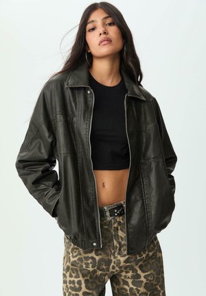 Sort læderjakke med krave-design, lynlås lukning og løst fit; båret over en sort cropped top og parret med leopardtryk bukser.