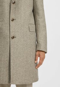 Beige checkered coat made of textured wool blend, featuring a five-button closure, side pocket, and slightly tailored silhouette.