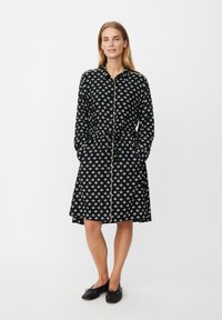 Czarna sukienka z powtarzającym się białym wzorem małych kształtów, długimi rękawami, zapinana na guziki z przodu, z wiązanym w talii paskiem oraz bocznymi kieszeniami.
