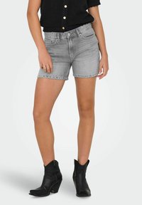 Shorts en denim gris clair avec une coupe décontractée, dotés d'un ourlet effiloché, de poches, associés à des bottines noires et un haut en tricot noir.