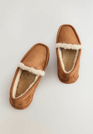 Tan suede pantoffels met een zachte, pluffy witte voering, geplaatst op een lichte achtergrond, die hun comfortabele ontwerp en ronde vorm laten zien.
