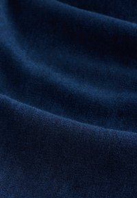 Dunkelblauer Samtstoff mit einer weichen, glatten Textur, die subtile Variationen in Glanz und Tiefe aufweist und elegant in Falten fällt.