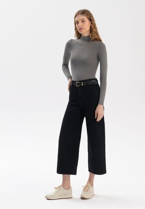 Maglione grigio a maniche lunghe, colletto alto, abbinato a jeans neri a gamba larga e sneakers beige. Gli outfit presentano texture lisce e un design sobrio.