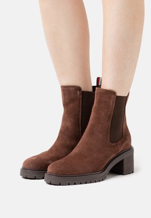 Bottines en daim marron avec panneaux latéraux élastiques, talon bloc texturé et semelle en caoutchouc. Comprend une lanière décorative tirante rouge, blanche et bleue.