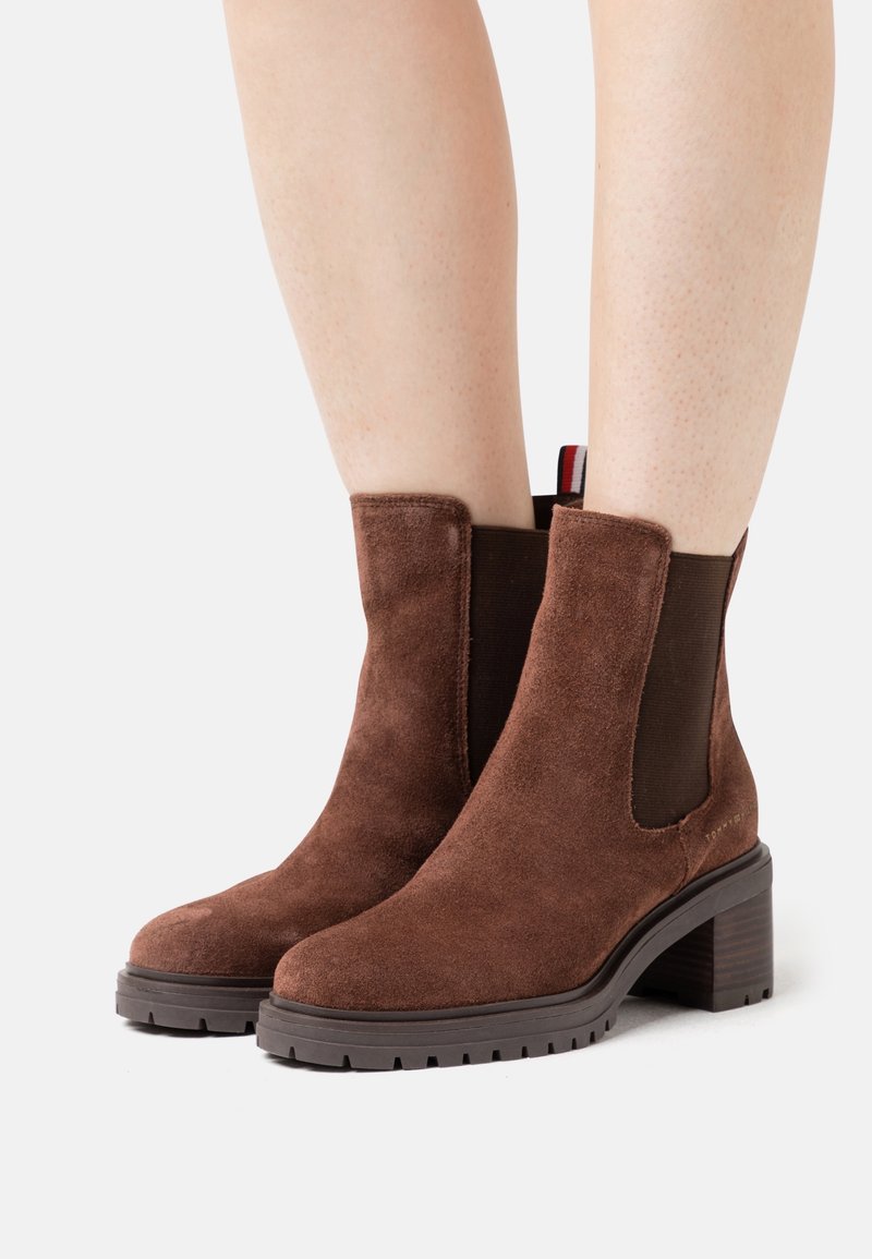 Bottines en daim marron avec panneaux latéraux élastiques, talon bloc texturé et semelle en caoutchouc. Comprend une lanière décorative tirante rouge, blanche et bleue.