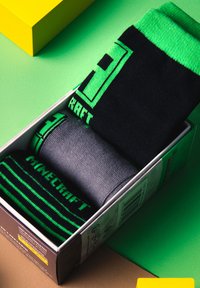Three pairs of socks in a box: one black with green accents and logo, one solid gray, and one with black and green stripes.