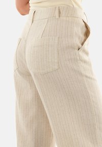 Pantaloni a righe beige con vita alta, texture morbida e due tasche posteriori. Presentano righe verticali per un aspetto sartoriale.