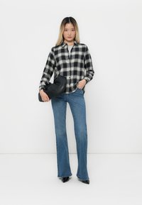 Svarte og hvite rutete skjorter, høyt liv blå vide jeans og svart håndveske. Glatt stoff med knapper og lange ermer.