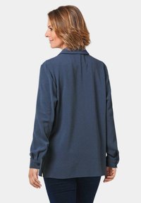 Marineblaue Langarmbluse mit Kragen und geknöpften Manschetten, mit glatter Textur und lockerer Passform. Sichtbare Seitenschlitze am Saum.