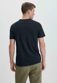 Grijze T-shirt met ronde hals en korte mouwen, gemaakt van zacht katoen. Eenvoudig ontwerp, geen patronen of afbeeldingen, gedragen met olijfgroene broek.