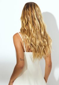 Valkoinen mekko ohuilla olkaimilla, sileä pinta ja napakka muotoilu. Pitkä, laineikas vaaleanblondi tukka; selkä-tatuointi koirasta. Minimalistinen tausta.