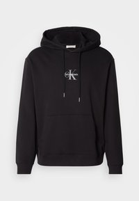 Sudadera de algodón negra con capucha ajustable, bolsillo canguro y un logo plateado con "Calvin Klein" y "CK" en el pecho.