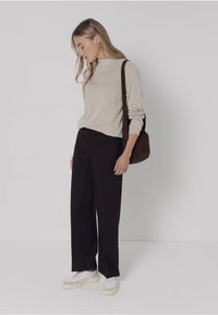 Pull en maille beige, pantalon large noir et baskets blanches. Sac à main marron. Mannequin se tient de profil sur un fond neutre.