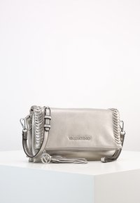 Stříbrná kožená crossbody kabelka s opleteným detailem na bocích, zipovým uzávěrem, odnímatelným popruhem a střapcem jako dekorací. Na přední straně logo "Valentino".