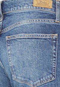 Jeans de mezclilla con un lavado azul claro, costuras clásicas, un bolsillo trasero con un parche de cuero y un acabado suave y texturizado.