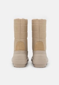 Botas de rodilla color beige con un diseño de tela acolchada, acentos de ante y una suela de goma texturizada. Acabado suave y borde superior redondeado.