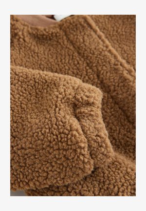 Material de pluș maro cu suprafață moale și texturată, având o senzație ușor groasă și pufoasă, cu detalii vizibile de cusături.