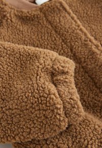 Tissu en polaire marron avec une surface douce et texturée, présentant une sensation légèrement épaisse et pelucheuse ainsi que des détails de couture visibles.