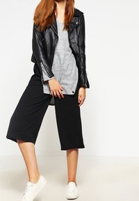 Giubbotto da moto in pelle nera, top in maglia grigia, culottes nere e sneakers bianche; si concentra su trame sovrapposte ed elementi di design casual.