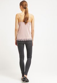 Világos rózsaszín selyem camisole állítható pántokkal és fodros csipkebetéttel az alján, sötétszürke skinny farmernadrággal és fekete lapos cipőkkel párosítva.