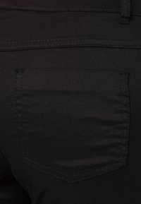 Gros plan d'une poche arrière en tissu noir sur un jean en denim avec des coutures visibles et une boucle de ceinture en haut.