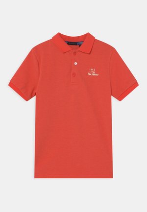 Czerwona koszulka polo z krótkim rękawem, kołnierzykiem, trzema guzikami oraz małym białym logo i napisem „IKKS” na lewej piersi.