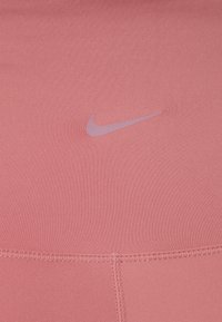 Top sportivo rosa realizzato in un tessuto morbido e elasticizzato, con un piccolo logo Nike lilla e dettagli di cuciture piatte.
