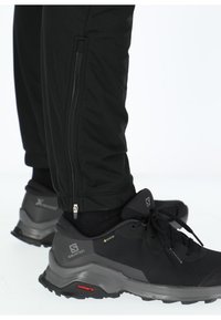 Zwarte sportbroek met zijritsen in combinatie met zwarte waterdichte schoenen met gestructureerde stof en dikke rubberen zolen.