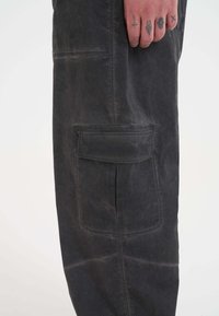 Pantaloni cargo neri con una finitura sfumata e texture. Presentano una tasca laterale e dettagli di cucitura, offrendo un design rilassato e funzionale.