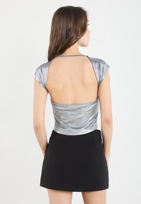 Top metálico plateado con mangas cortas y espalda baja, combinado con una mini falda negra. Textura suave con un diseño ajustado y mínimos detalles.