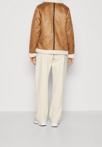 Brown faux shearling jacket with a zip closure, cream trim, and long sleeves, paired with cream wide-leg pants and white sneakers.