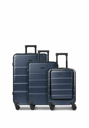 Tre valigie rigide blu navy con quattro ruote e maniglie telescopiche, disposte in ordine decrescente di dimensioni su sfondo bianco.