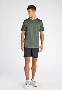 Maglietta a maniche corte verde scuro con "LINDBERGH" stampato sul davanti, abbinata a pantaloni shorts blu navy e scarpe da ginnastica bianche. Tessuto liscio, vestibilità atletica.