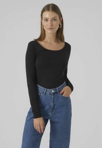Haut noir à manches longues avec un décolleté large, associé à un jean en denim bleu taille haute. Le tissu semble doux et ajusté.