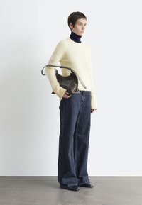 Helles gelbes Sweatshirt, dunkelblauer Rollkragenpullover, lockere dunkle Jeans und eine geflochtene braune Handtasche. Die Schuhe sind schwarz mit spitzer Spitze. Einfaches, modernes Design.