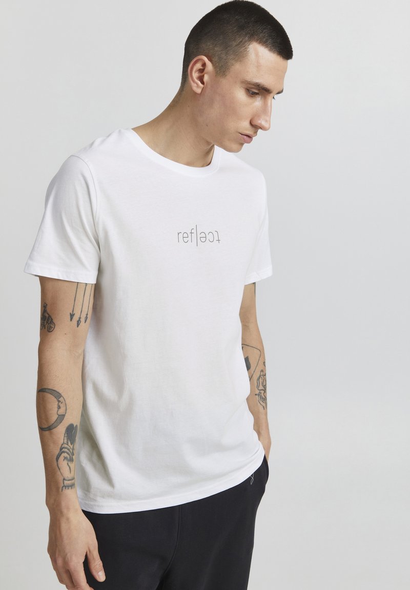 Hvid kortærmet t-shirt lavet af bomuld med en rund halsudskæring. Har et trykt logo, "reflect," i en kontrastfarve foran.