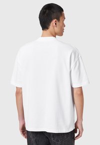 Camiseta de algodón blanca con un corte holgado, cuello redondo y mangas cortas, que presenta una textura suave y un diseño en color sólido.