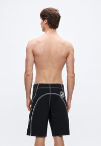 Μαύρα βερμούδα για παραλία με λευκή ραφή και �λογότυπο, σχεδιασμένα με άνετη εφαρμογή και μήκος μέχρι το γόνατο. Χωρίς ορατά σχέδια ή διακοσμητικά στοιχεία.